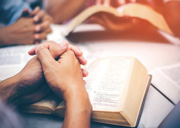 Group of hands praying over Bibles